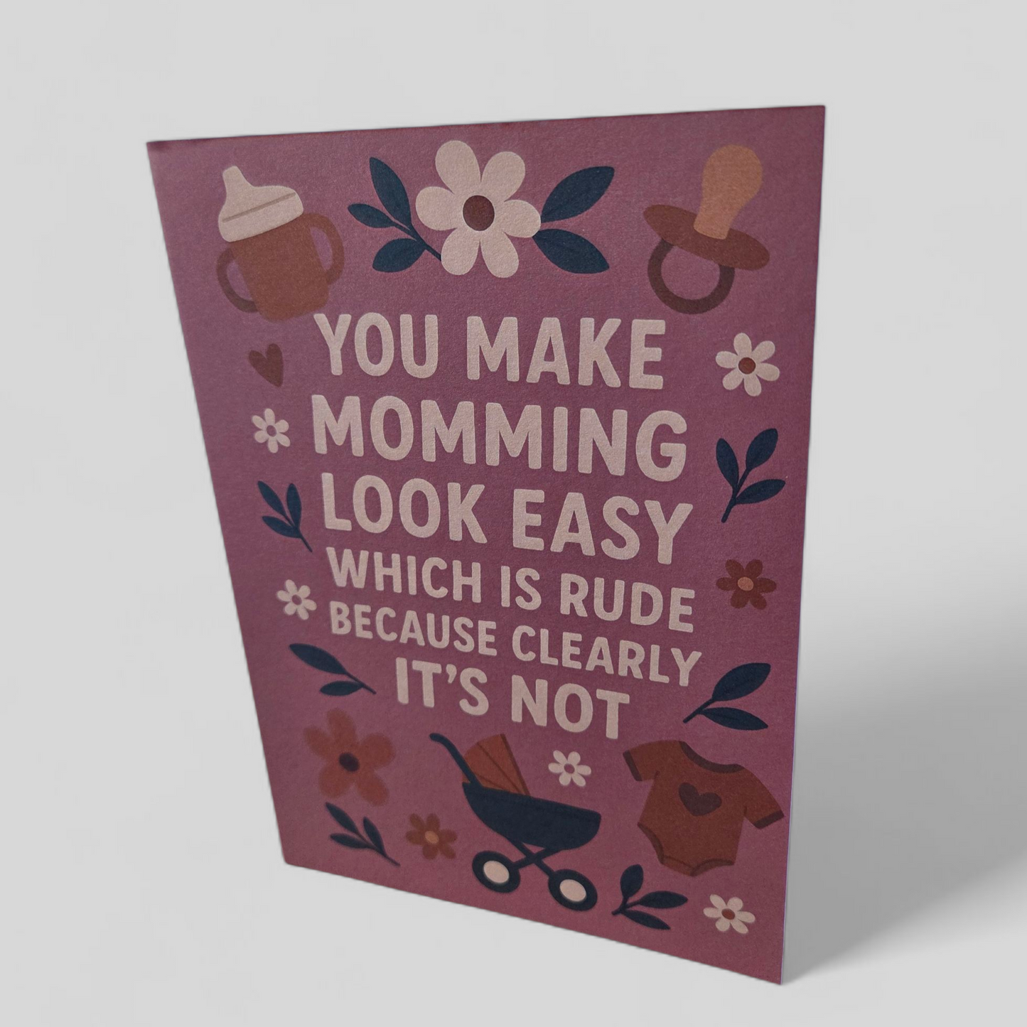 Greeting card reading ‘You make momming look easy which is rude because clearly it’s not’ with pink background and floral accents.