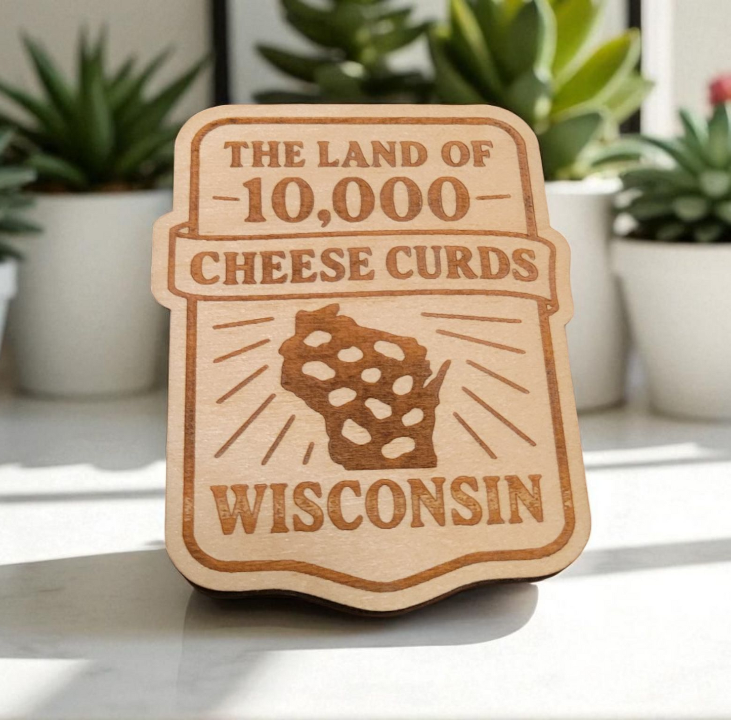 Laser-cut wooden Wisconsin magnet that reads “The Land of 10,000 Cheese Curds” with a cheese-curd-shaped state outline, styled on a badge shape.