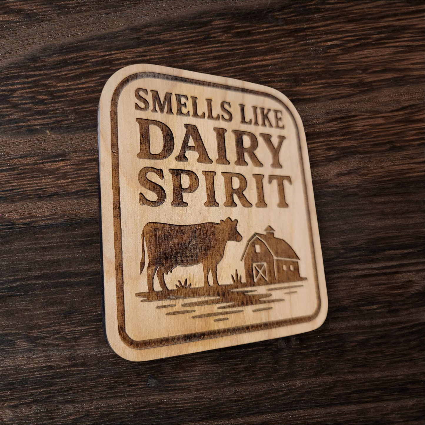 Laser-engraved wood magnet with cow and barn design, captioned “Smells Like Dairy Spirit”