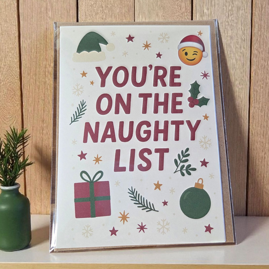 Greeting card reading ‘You’re on the Naughty List’ with Santa hat emoji, holly, ornaments, and stars.