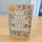 Greeting card reading ‘You Make Life Feel Like Sunshine’ with smiling suns and floral design.