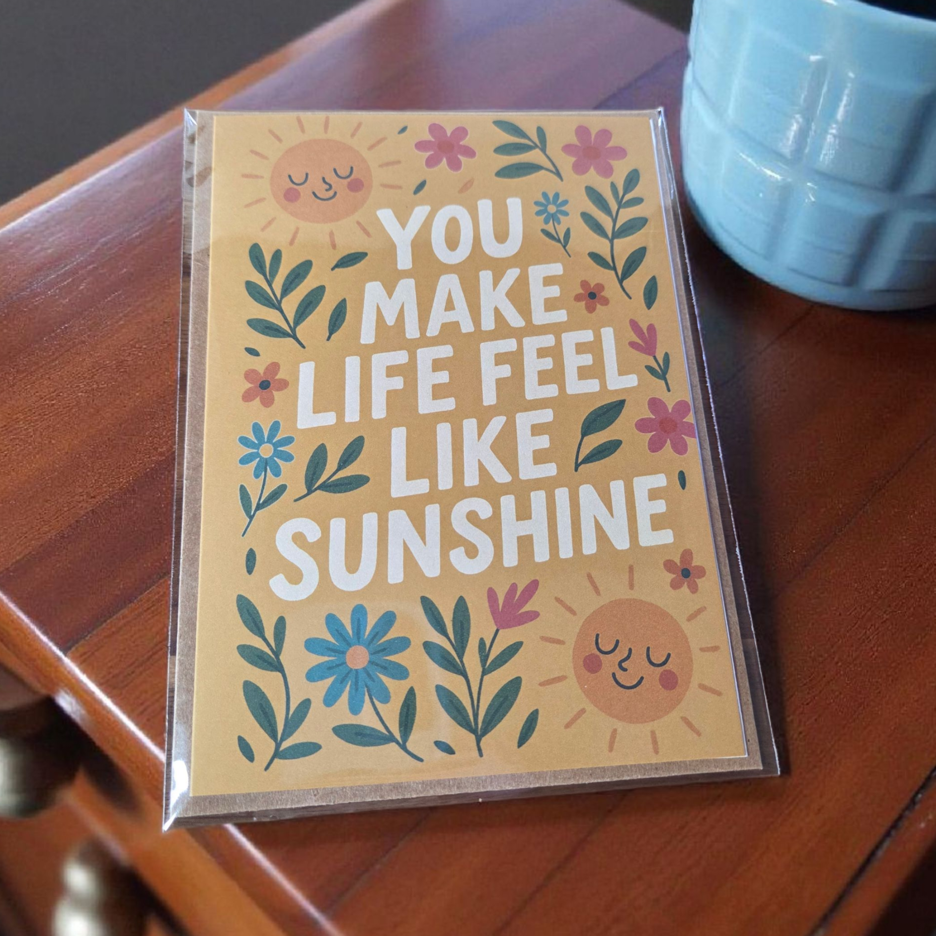 Greeting card reading ‘You Make Life Feel Like Sunshine’ with smiling suns and floral design.