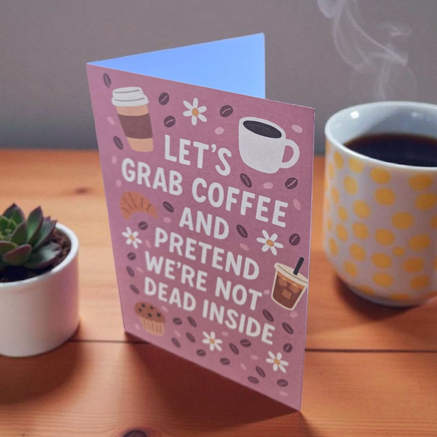Greeting card reading ‘Let’s Grab Coffee and Pretend We’re Not Dead Inside’ with coffee and pastry illustrations.