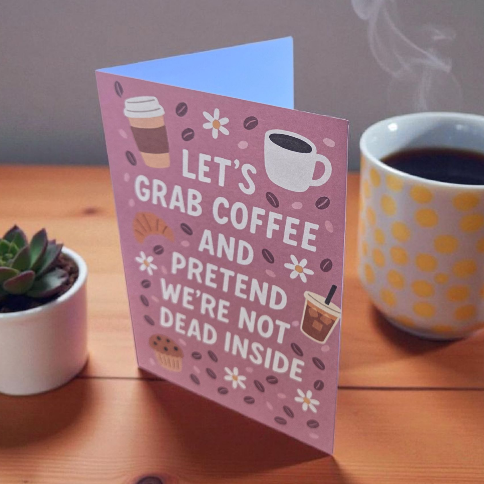 Greeting card reading ‘Let’s Grab Coffee and Pretend We’re Not Dead Inside’ with coffee and pastry illustrations.