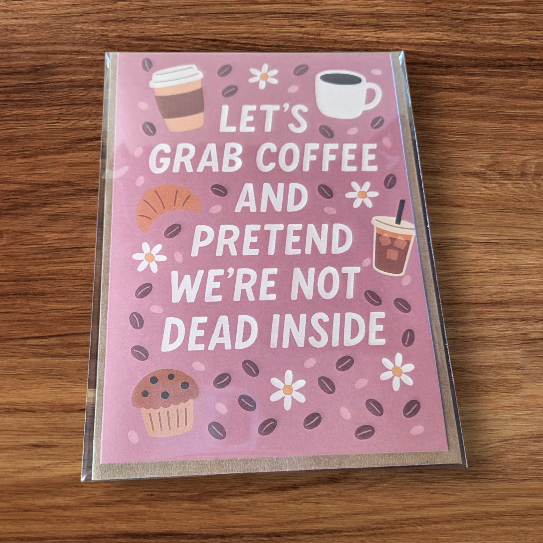 Greeting card reading ‘Let’s Grab Coffee and Pretend We’re Not Dead Inside’ with coffee and pastry illustrations.