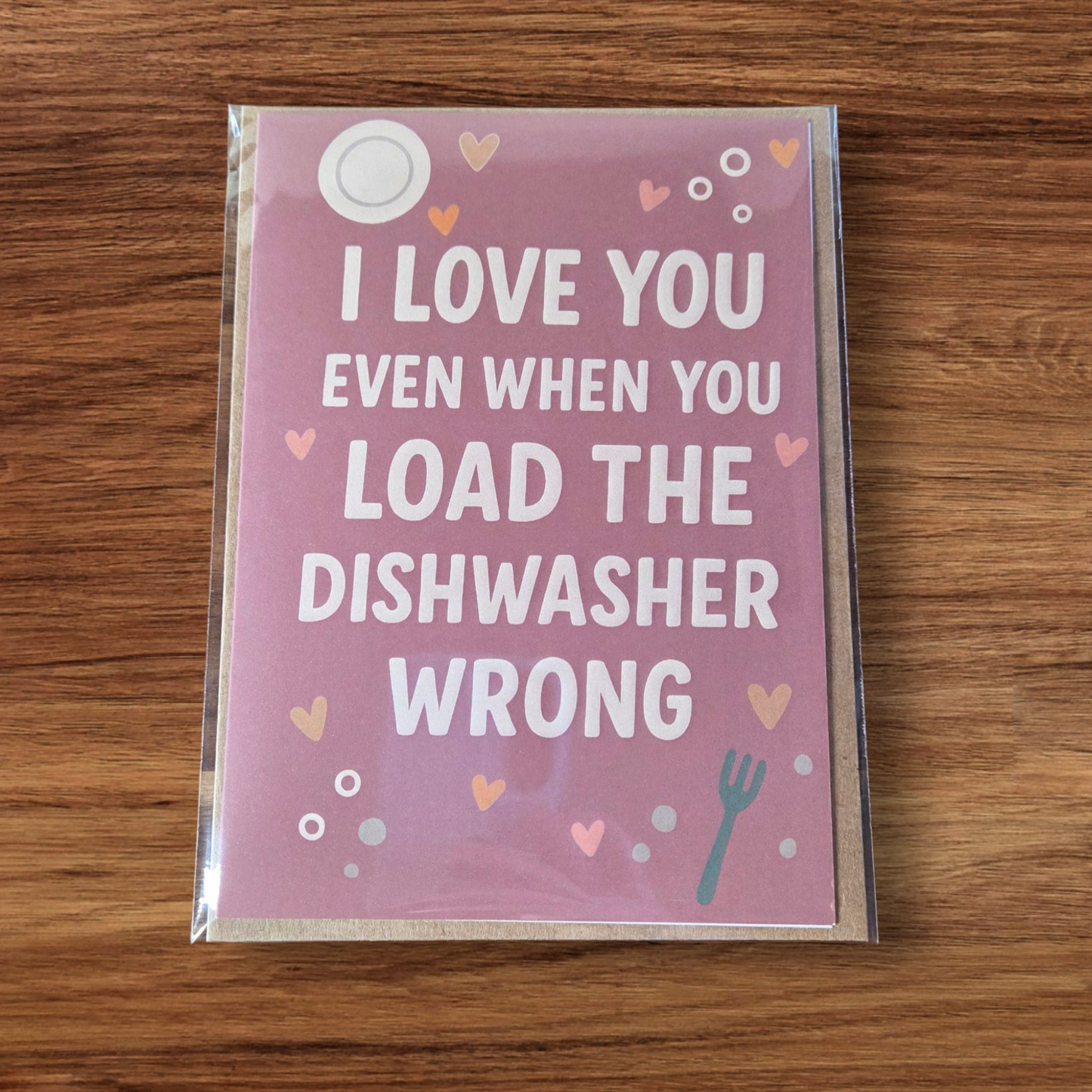 Funny greeting card reading ‘I Love You Even When You Load the Dishwasher Wrong’ on pink background with hearts.
