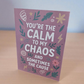 Greeting card reading ‘You’re the Calm to My Chaos and Sometimes the Cause’ on mauve background with floral and lightning illustrations.