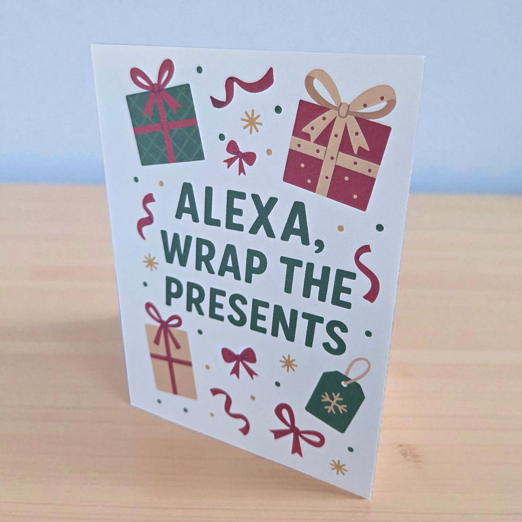 Funny Christmas greeting card reading ‘Alexa, Wrap the Presents’ surrounded by wrapped gift illustrations.