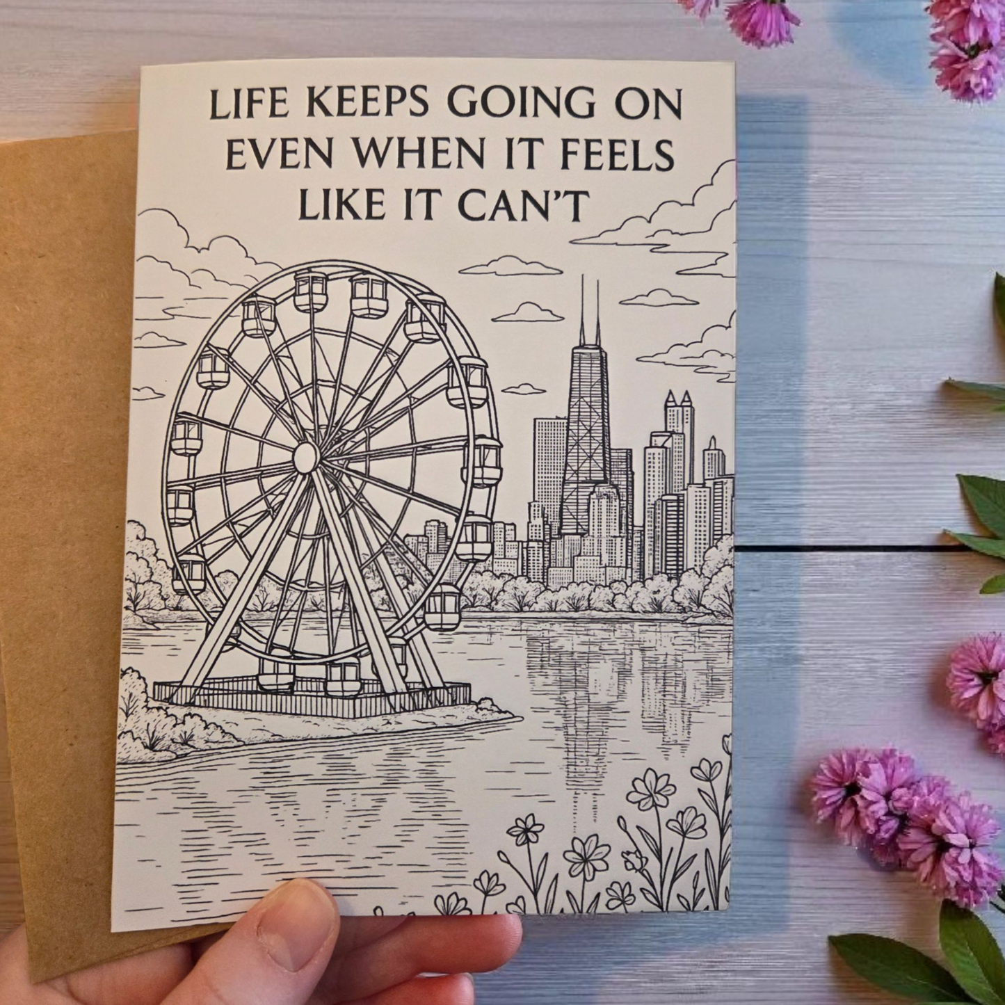 Black-and-white greeting card reading ‘Life Keeps Going On Even When It Feels Like It Can’t’ featuring a ferris wheel and city skyline.