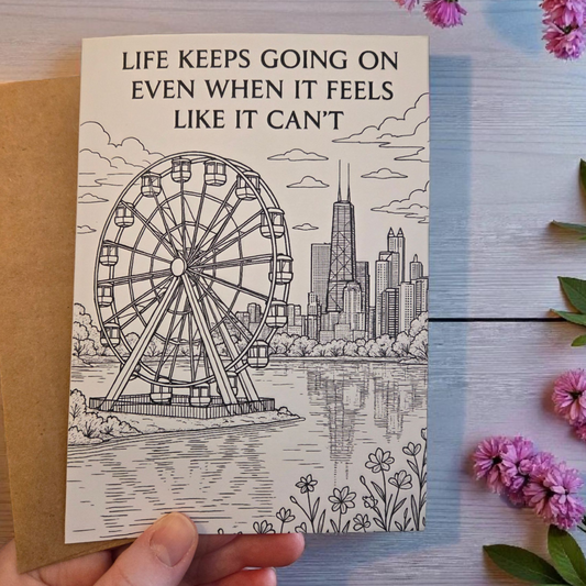 Black-and-white greeting card reading ‘Life Keeps Going On Even When It Feels Like It Can’t’ featuring a ferris wheel and city skyline.