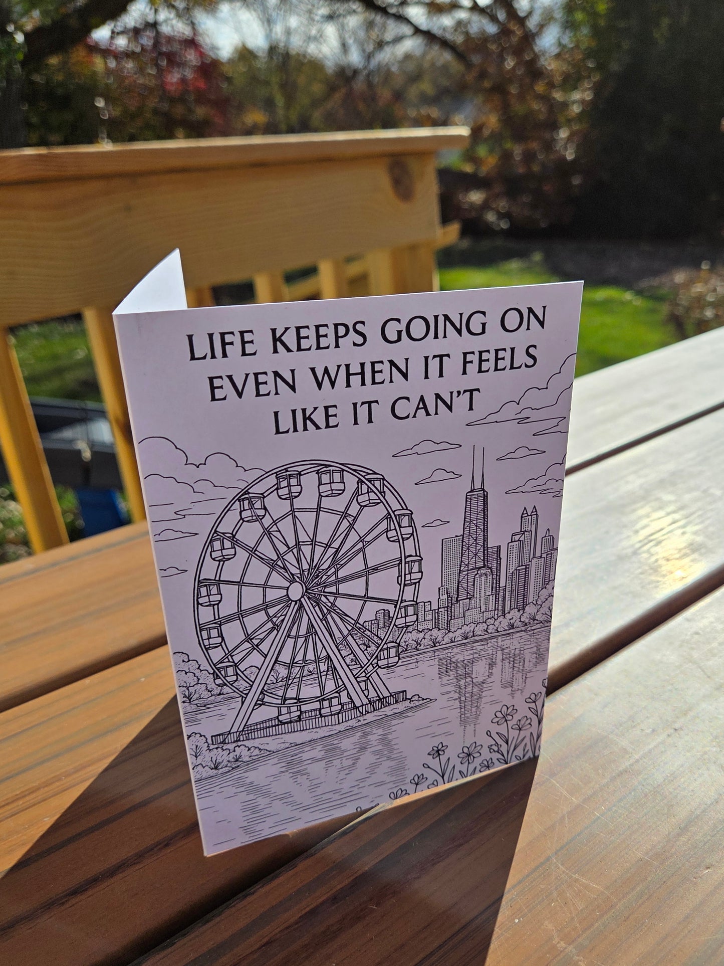 Black-and-white greeting card reading ‘Life Keeps Going On Even When It Feels Like It Can’t’ featuring a ferris wheel and city skyline.