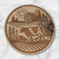 Laser-engraved round wooden magnet featuring a Holstein cow in a rural farm scene with barn, silo, and sun – rustic Wisconsin farmhouse decor by Ellie Joe Design Co.