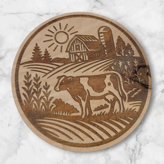 Laser-engraved round wooden magnet featuring a Holstein cow in a rural farm scene with barn, silo, and sun – rustic Wisconsin farmhouse decor by Ellie Joe Design Co.