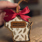 Handcrafted Wisconsin-shaped botanical wood ornament personalized with Janesville, Wisconsin on a leather accent and finished with a wine-red bow and leather hanger.