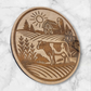 Laser-engraved round wooden magnet featuring a Holstein cow in a rural farm scene with barn, silo, and sun – rustic Wisconsin farmhouse decor by Ellie Joe Design Co.