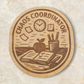 Laser engraved Chaos Coordinator wood magnet featuring teacher desk scene with open planner, apple, pencils, sticky notes, and clock
