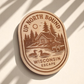 Wood magnet engraved with a lakeside cabin, pine trees, loons, and the words “Up North Bound – Wisconsin Escape.”