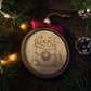 Handcrafted layered wood Christmas ornament featuring an engraved raccoon in a festively decorated trash can holding a “festive but feral” sign, finished with a wine-red bow, wood bead, and leather hanging loop.
