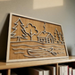 Layered wood sign featuring a rustic cabin, pine trees, and canoe scene — laser cut from multiple layers of natural wood, perfect for lake house or cabin decor.