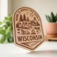 Wood magnet engraved with camper, pine trees, and fire pit, and the phrase “Home is where you park it – Wisconsin.”